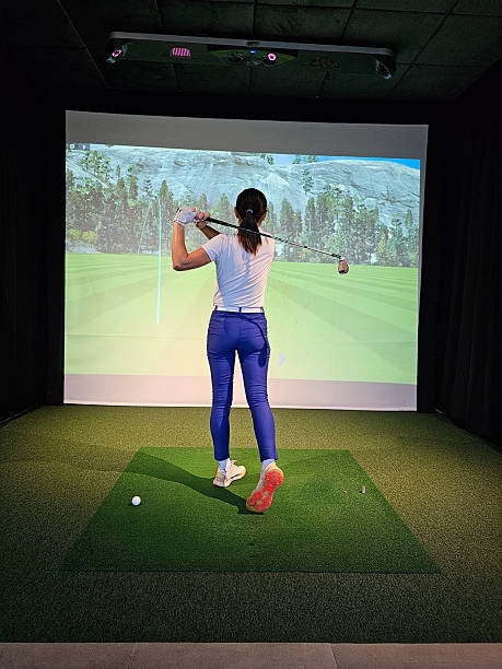 Woman practicing golf swing indoors at a virtual simulator with projected scenery in the background